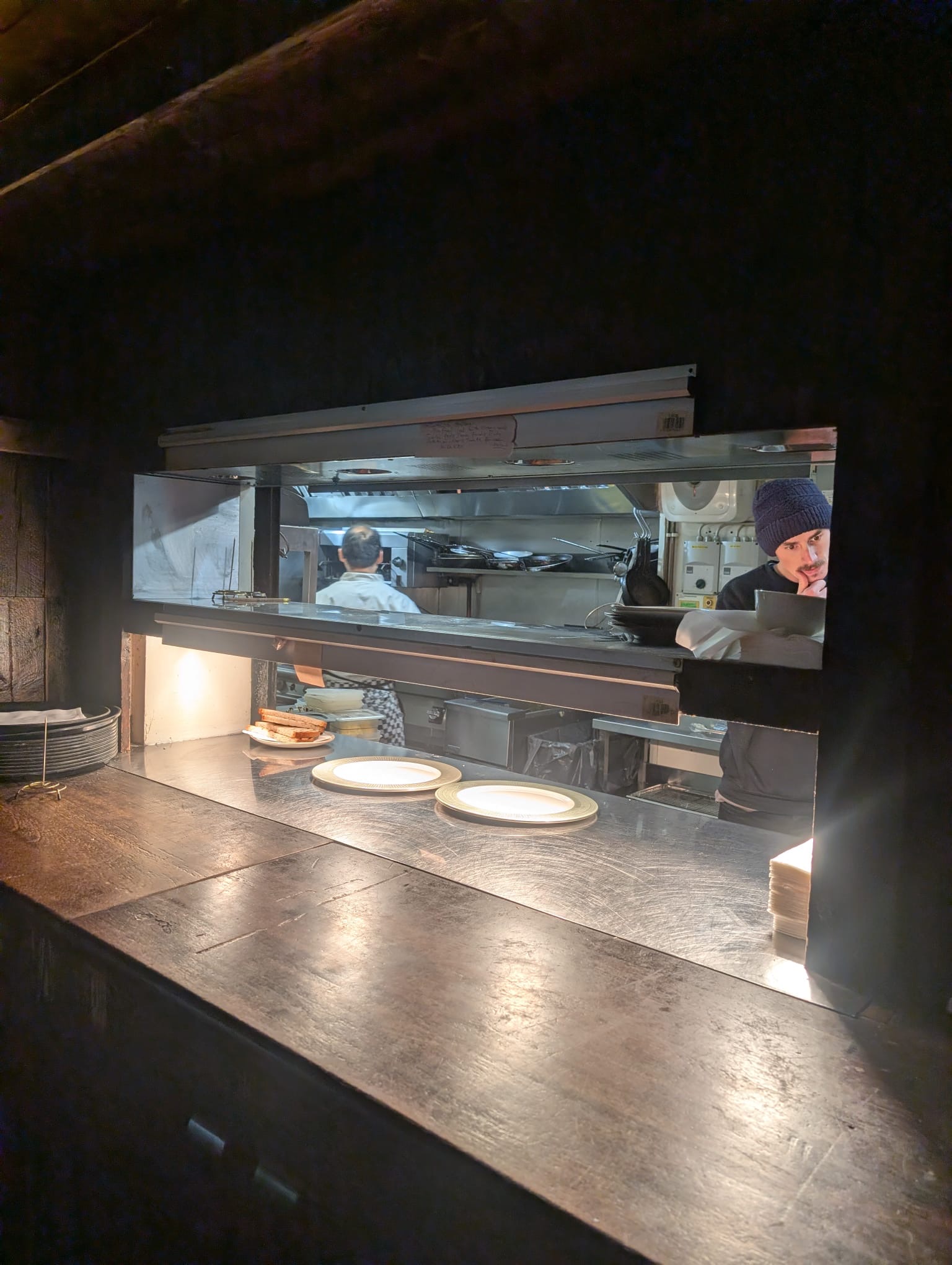 Dark roller shutter raised above a stainless-steel kitchen-pass counter in a Dublin restaurant, with the kitchen visible behind